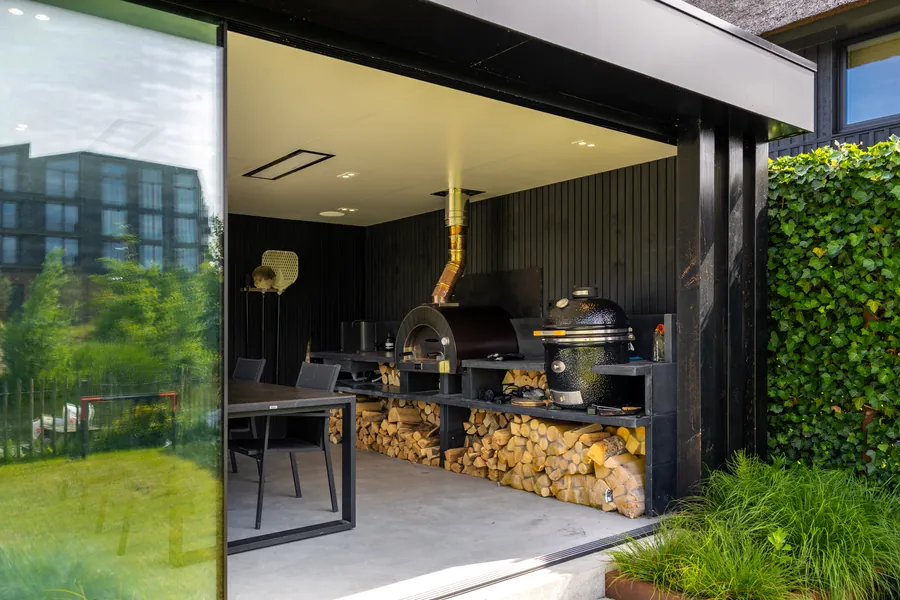 Buitenkeuken met pizzaoven en kamado in een zwart houten bijgebouw, gebouwd door Bax Hoveniers
