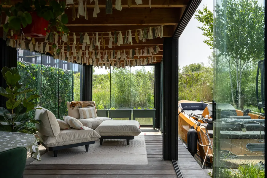 Tuinkamer met glazen wanden en loungebank, met zicht op het water