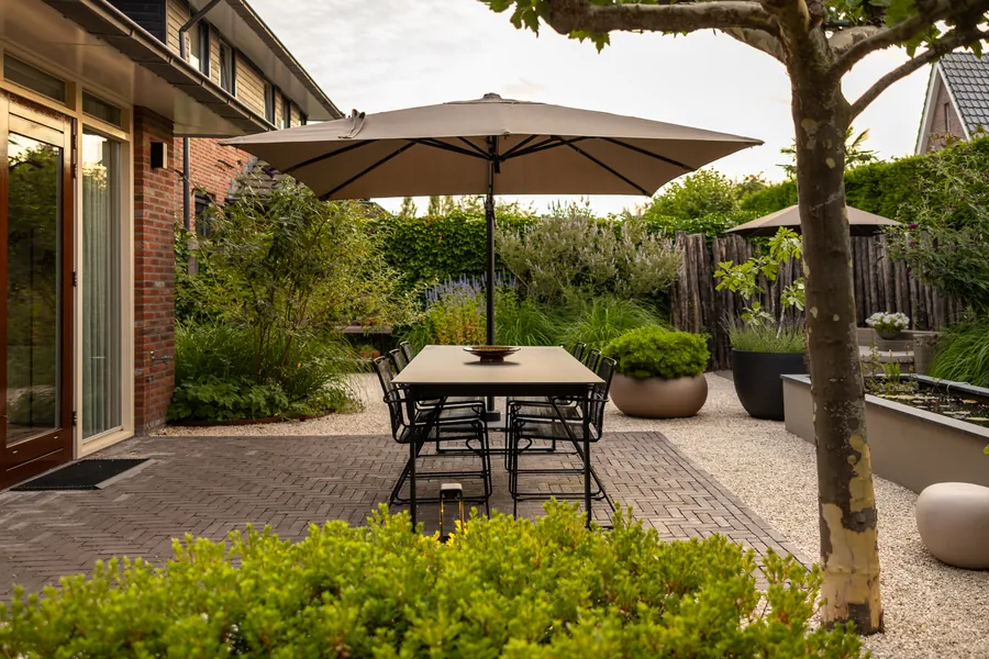 Verzorgd terras met eettafel, parasol en strak gesnoeide beplanting