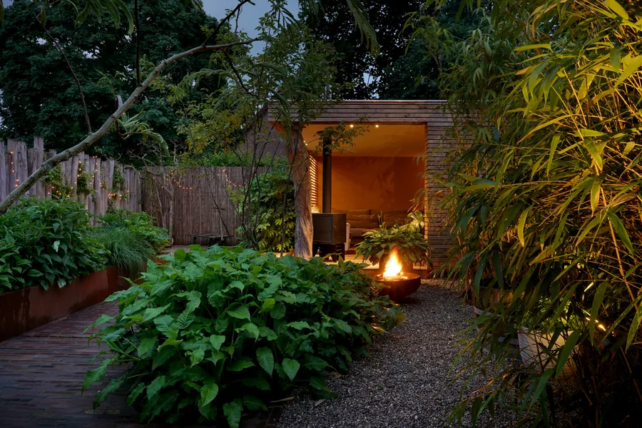 Houten paviljoen met vuurschaal tussen weelderige beplanting